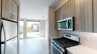 Located on NE Martin Luther King Jr Boulevard in Portland's vibrant Northeast neighborhood, this single-floor unit features a contemporary design with a clean, neutral palette throughout. Light wood-tone flooring runs consistently across the living areas, enhancing the sense of openness and cohesion.

The kitchen is well-appointed with flat-front cabinetry in a warm wood-grain finish, light quartz countertops, a white tile backsplash, and a full suite of stainless steel appliances including a gas range, over-the-range microwave, and dishwasher. The layout flows naturally toward the living area, which is anchored by a pair of large floor-to-ceiling windows that flood the space with natural light and offer views of the surrounding Portland streetscape and neighboring buildings.

A dedicated area within the unit accommodates a stacked washer and dryer, providing convenient in-unit laundry. The bathroom features a full tub-shower combination with chrome fixtures and wood-look flooring, maintaining the unit's consistent modern aesthetic.

Throughout the space, neutral warm-gray walls, clean white trim, and abundant natural light contribute to a bright, contemporary atmosphere well-suited to urban living in Northeast Portland.