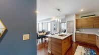 Located in Ballston Spa, NY, this two-bedroom, two-bathroom single-floor residence offers a thoughtfully designed open-concept layout with rich hardwood-style flooring flowing throughout the main living areas. The kitchen is a functional centerpiece, featuring light wood cabinetry, granite countertops, stainless steel appliances including a range, microwave, and refrigerator, and a large island with pendant lighting and seating — ideal for casual dining or entertaining. The kitchen opens seamlessly into the dining area and living room, where bold teal accent walls create a striking visual contrast against the neutral tones. The living room receives natural light through multiple windows and includes direct access to an exterior door. The generously sized primary bedroom features wide windows with sheer curtains, carpet flooring, and an en-suite bathroom complete with a walk-in glass shower and wood-toned vanity with granite countertops. The second bedroom is carpeted and equally well-lit. A second full bathroom offers a tub-shower combination and matching granite vanity. A dedicated laundry room with full-size washer and dryer adds everyday convenience, completing this well-balanced and stylishly finished residence.