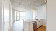 Located on the 11th floor of 333 E Superior Street in Duluth, Minnesota, this 2-bedroom, 2-bathroom residence offers a refined modern aesthetic with striking architectural details throughout. Exposed concrete ceilings lend an industrial character to the space, contrasting elegantly with light-toned hardwood-style flooring that runs continuously throughout each room.

The open-concept kitchen and living area serves as the heart of the home, featuring a large quartz-topped island with an integrated sink, white cabinetry extending to the ceiling, subway tile backsplash, and stainless steel appliances. Floor-to-ceiling sliding glass doors in the living area lead to a private balcony with sweeping views of Lake Superior.

Both bedrooms are generously proportioned, each benefiting from large windows that frame panoramic water and cityscape views, filling the rooms with abundant natural light. The primary bedroom features corner floor-to-ceiling windows offering exceptional lake views.

The two bathrooms are finished with clean, contemporary details. The primary bath includes a frameless glass walk-in shower with vertical white subway tile, while the second bathroom offers a full soaking tub with matching tile surround and a backlit vanity mirror. A hallway connects the bedrooms and provides access to two dedicated closets, completing this well-designed urban residence.