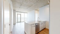 Located on the 11th floor of 333 E Superior Street in Duluth, Minnesota, this 2-bedroom, 2-bathroom residence offers a refined modern aesthetic with striking architectural details throughout. Exposed concrete ceilings lend an industrial character to the space, contrasting elegantly with light-toned hardwood-style flooring that runs continuously throughout each room.

The open-concept kitchen and living area serves as the heart of the home, featuring a large quartz-topped island with an integrated sink, white cabinetry extending to the ceiling, subway tile backsplash, and stainless steel appliances. Floor-to-ceiling sliding glass doors in the living area lead to a private balcony with sweeping views of Lake Superior.

Both bedrooms are generously proportioned, each benefiting from large windows that frame panoramic water and cityscape views, filling the rooms with abundant natural light. The primary bedroom features corner floor-to-ceiling windows offering exceptional lake views.

The two bathrooms are finished with clean, contemporary details. The primary bath includes a frameless glass walk-in shower with vertical white subway tile, while the second bathroom offers a full soaking tub with matching tile surround and a backlit vanity mirror. A hallway connects the bedrooms and provides access to two dedicated closets, completing this well-designed urban residence.