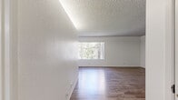 Located at 2561 Madera Cir, Unit 28 in Port Hueneme, CA, this single-story, one-bedroom, two-bathroom residence offers a thoughtfully organized layout with a clean, neutral aesthetic throughout. The combined kitchen and living area forms the heart of the home, where wood-style flooring runs underfoot and large windows invite generous natural light and outdoor greenery views. The kitchen features white cabinetry, a peninsula with a light granite-style countertop, a range hood, and black appliances including a full-size refrigerator. The open living area is bright and airy, with a textured ceiling and easy access to the front entry. The bedroom is carpeted for comfort and includes a sizable window with outdoor views, providing a quiet retreat. The primary bathroom is well-appointed with a wide vanity, ample cabinetry, a large mirror with overhead lighting, and wood-style flooring. A second bathroom features a shower/tub combination. A connecting hallway ties the spaces together efficiently. The overall ambiance is light, clean, and functional, well-suited for comfortable everyday living in coastal Southern California.