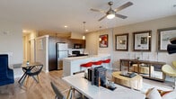 Located at 888 E 66th St in Indianapolis, Indiana, this thoughtfully designed one-bedroom, one-bathroom residence offers a well-appointed single-floor layout with a clean, contemporary aesthetic throughout. The open-concept kitchen and living room serves as the heart of the unit, anchored by a striking quartz waterfall island with an undermount sink and bar seating. The kitchen features dark espresso cabinetry, stainless steel refrigerator, and black appliances, all complemented by pendant lighting overhead. The living area is bathed in natural light from large windows and a sliding glass door that opens to a private balcony with open neighborhood views. A ceiling fan adds comfort to the airy living space. Light wood-style flooring runs throughout the main living areas, creating a cohesive and modern feel. A hallway with recessed lighting connects the main living space to the private bedroom, bathroom, and closet. The carpeted bedroom is a comfortable retreat, featuring a ceiling fan and direct access to a dedicated closet with built-in shelving. The bathroom is finished with a dark vanity, granite countertop, and light wood-style flooring, maintaining the modern design language found throughout. The unit offers a well-balanced combination of style, functionality, and natural light.