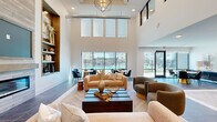 This contemporary clubhouse at 209 W Interstate 20 offers a thoughtfully designed single-floor layout that seamlessly integrates a living room, dining area, and kitchen into one cohesive and inviting space. The living area commands attention with dramatically soaring ceilings, a sleek linear fireplace set against a wood-panel surround, and built-in shelving that adds warmth and character. Large-format stone tile flooring transitions to a striking herringbone wood pattern, grounding the open layout with visual texture. A geometric chandelier anchors the living space, complemented by an abundance of natural light pouring in through expansive floor-to-ceiling windows that frame views of the outdoor pool and surrounding community. The dining area benefits directly from this pool-facing glazing, with direct access to the exterior through glass-panel doors. The kitchen features dark wood cabinetry, a large central island with a mosaic tile base, open floating shelves, a glossy white tile backsplash, under-counter wine storage, and pendant lighting. A vestibule entry with black-framed glass partition doors provides an elegant transition into the main space. Throughout, the design maintains a clean, upscale aesthetic defined by neutral tones, curated décor, and high-quality materials.