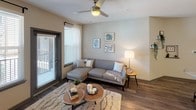 This single-floor residential unit offers a thoughtfully designed layout combining modern finishes with comfortable living spaces throughout. The kitchen is a standout feature, showcasing crisp white shaker cabinetry, granite countertops, a subway tile backsplash, stainless steel appliances, and a central island that provides additional prep space and seating. Wood-look flooring runs through the kitchen and main living areas, adding warmth and visual continuity. The living room is bright and inviting, benefiting from natural light through a sliding glass door that opens to an outdoor balcony, complemented by a ceiling fan overhead. The primary bedroom is generously sized with plush carpeting, a ceiling fan, and windows that invite natural light. It is served by a well-equipped full bathroom featuring a dual-sink vanity with granite countertops, wood-look flooring, and a tiled tub-shower combination. The second bedroom also features carpet flooring, a ceiling fan, and a window with exterior views. Its adjacent bathroom mirrors the refined finishes of the primary bath, complete with a granite vanity, tiled shower-tub surround, and wood-look flooring. Throughout the unit, neutral wall tones, consistent trim details, and quality finishes create a cohesive and comfortable living environment.