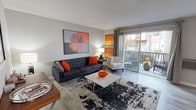 This single-floor residence offers a thoughtfully designed layout that balances comfort and functionality across its key living spaces. The living room serves as the heart of the unit, featuring light hardwood-style flooring, neutral grey walls, and sliding glass doors that open onto a private balcony, filling the space with natural light and providing outdoor views. Bold artwork and contemporary furnishings lend the room a modern, mid-century aesthetic.

Adjacent to the living area, the dining space accommodates a round glass-top table beneath a ceiling fan, with a window overlooking the surroundings. The galley-style kitchen is efficiently arranged with white cabinetry, dark countertops, stainless steel appliances, and continued hardwood-style flooring, with a clear sightline leading toward the rest of the unit.

The bedrooms are carpeted and well-lit by broad windows fitted with draping curtains. Each room offers a calm, restful atmosphere with neutral tones and baseboard heating. Closet space is present, and the rooms comfortably accommodate full-sized furniture.

Overall, the unit presents a cohesive, contemporary aesthetic with consistent finishes, practical layouts, and a warm, inviting ambiance throughout.