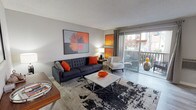 This single-floor residence offers a thoughtfully designed layout that balances comfort and functionality across its key living spaces. The living room serves as the heart of the unit, featuring light hardwood-style flooring, neutral grey walls, and sliding glass doors that open onto a private balcony, filling the space with natural light and providing outdoor views. Bold artwork and contemporary furnishings lend the room a modern, mid-century aesthetic.

Adjacent to the living area, the dining space accommodates a round glass-top table beneath a ceiling fan, with a window overlooking the surroundings. The galley-style kitchen is efficiently arranged with white cabinetry, dark countertops, stainless steel appliances, and continued hardwood-style flooring, with a clear sightline leading toward the rest of the unit.

The bedrooms are carpeted and well-lit by broad windows fitted with draping curtains. Each room offers a calm, restful atmosphere with neutral tones and baseboard heating. Closet space is present, and the rooms comfortably accommodate full-sized furniture.

Overall, the unit presents a cohesive, contemporary aesthetic with consistent finishes, practical layouts, and a warm, inviting ambiance throughout.
