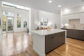 Located in Santa Ana, CA, this two-story residence offers a thoughtfully designed open-concept layout across two floors. The main level is expansive, anchored by a dramatic double-height living area flooded with natural light through floor-to-ceiling windows and transom glass. Light wood-tone flooring flows throughout, complementing the bright white walls and creating a clean, contemporary aesthetic.

The kitchen is a standout feature, boasting white upper cabinetry, warm-toned lower cabinets, a large quartz waterfall island with bar seating, stainless steel appliances including a gas range, built-in microwave, French door refrigerator, and dishwasher — all finished with under-cabinet lighting and crisp white countertops.

Both bathrooms are finished in a consistent modern palette, featuring quartz vanity tops, warm wood-toned cabinetry, brushed nickel fixtures, and a tub-shower combination with subway tile surrounds.

The upper floor houses the generously sized primary bedroom, a serene retreat with light-filled windows, soft neutral tones, and ample space. A secondary lounge or sitting area on the upper level adds flexibility to the floor plan. A staircase with modern railing connects both levels, reinforcing the home's contemporary character throughout.