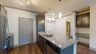 This single-floor residence offers a thoughtfully designed layout that balances style and functionality throughout. The heart of the home is an open-concept kitchen showcasing rich dark cabinetry, striking granite countertops, and a generous island with seating overhang. Stainless steel appliances, a classic subway tile backsplash, and a built-in dishwasher complete the culinary space. Elegant cylindrical pendant lights hang above the island, while recessed and track lighting illuminate the area with warm, even light. Wood-look flooring runs throughout the main living and kitchen areas, adding warmth and continuity. The living area benefits from vaulted ceilings that lend a sense of openness and volume, with natural light streaming in through large windows fitted with blinds. A graceful arched doorway connects the main living space to adjacent rooms, adding an architectural detail that enhances the overall flow. One bedroom features vaulted ceilings, a built-in bookshelf, and windows overlooking lush greenery, while another offers plush carpeting and dual windows framing outdoor tree views. The bathroom is fitted with tile flooring, a tub-shower combination, and dark cabinetry with granite countertops, maintaining a consistent, cohesive design aesthetic throughout the home.