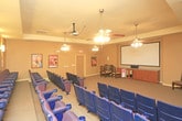 Located at 1102 N Memphis Ave in Lubbock, Texas, this single-floor private screening room delivers an authentic cinema experience within an intimate, well-appointed setting. The space is anchored by a large projection screen mounted at the front of the room, flanked by wall-mounted speakers and supported by a media console and cabinetry beneath. Two ceiling fans with integrated lighting fixtures are suspended from the tray ceiling, providing both air circulation and ambient illumination throughout the room.

The seating area features rows of plush, theater-style chairs with built-in cup holders, arranged in a tiered configuration to ensure clear sightlines to the screen from every seat. The warm, neutral-toned walls are adorned with a curated collection of framed classic Hollywood movie posters — including iconic titles such as Rear Window, The Wizard of Oz, High Noon, and Gone with the Wind — lending the space a nostalgic, cinematic character. Additional traditional wooden chairs are positioned along the side walls, offering flexible seating options.

The flooring is finished in a rich, dark carpet that complements the warm golden-beige wall tones and contributes to the room's acoustic quality. Overall, the space combines functional screening room design with classic film-inspired décor to create an inviting and immersive entertainment environment.