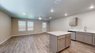 This two-story home is thoughtfully laid out across two floors, with the more compact ground level housing the primary living and kitchen areas, while the larger upper floor accommodates the bedrooms and additional bathrooms. The open-concept main floor seamlessly connects the kitchen and living room, both finished with light-toned wood-look flooring that runs consistently throughout the home. The kitchen is well-appointed with gray shaker-style cabinetry, white quartz countertops, stainless steel appliances including a refrigerator, range, microwave, and dishwasher, and a central island that provides additional prep and storage space. The living room receives natural light through multiple windows fitted with horizontal blinds, and a ceiling fan adds functionality to the space. An entry door with sidelight opens directly into this area. The attached garage features an automatic opener and concrete flooring, offering practical storage and parking. Upstairs, three bedrooms each include wood-look flooring and windows for natural light. The primary bedroom is generously sized and accompanied by a dedicated bathroom with a shaker-style vanity and a walk-in closet with built-in rods and shelving. Three additional closets and two hallways connect the upper-level spaces efficiently. A landscaped backyard with mature trees is visible from the exterior.