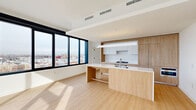 This thoughtfully designed residence offers a clean, modern aesthetic across a single floor, featuring 3 bedrooms, 5 bathrooms, and a seamless open-concept living and kitchen area. The combined kitchen and living room serves as the heart of the home, showcasing a striking island with a white quartz countertop, warm natural wood cabinetry, a gas cooktop, and a sleek linear pendant light overhead. Light hardwood flooring runs throughout, enhancing the bright, airy atmosphere. Expansive floor-to-ceiling windows flood the living area with natural light while framing sweeping panoramic city views, with access to an outdoor balcony that extends the living space further. The hallway connecting the bedrooms is clean and bright, finished in crisp white with recessed lighting. The bedrooms are well-proportioned and bathed in natural light; the primary bedroom features large windows with additional city views. The five bathrooms are finished in a contemporary style, with large-format grey tiles, glass-enclosed walk-in showers, dual undermount sinks, and expansive mirrors. A dedicated closet and hallway complete the layout, offering practical storage solutions. The overall ambiance is minimalist and sophisticated, with a consistent palette of white, warm wood, and neutral tones.