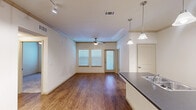 Located in Waller, Texas, this well-appointed 2-bedroom, 2-bathroom residence offers a thoughtful single-story layout that balances functionality and comfort. The open-concept living and dining area features rich wood-style flooring, a ceiling fan, and multiple windows fitted with blinds that allow natural light to fill the space, creating a bright and welcoming atmosphere.

The kitchen is a standout feature, centered around a peninsula island with a dark countertop and stylish pendant lighting overhead. Light wood cabinetry provides generous storage, while black appliances — including a refrigerator, range, and built-in microwave — add a sleek, cohesive look. Track lighting illuminates the workspace effectively.

Both bedrooms are carpeted and equipped with ceiling fans and windows, offering a comfortable, quiet retreat. The primary bedroom connects to a well-designed en-suite bathroom featuring a long vanity with dark countertops, warm wood cabinetry, a walk-in glass shower, and tile flooring. A second bathroom includes a full tub-shower combination with tile surround. Each bedroom is served by its own closet, with the primary featuring a spacious walk-in design complete with built-in shelving and dual hanging rods for organized storage.