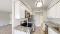 Located at 3314 Wickslow Dr in Wilmington, NC, this single-floor home offers a well-designed layout with a clean, modern aesthetic throughout. The kitchen is a standout feature, showcasing granite countertops, white shaker-style cabinetry, a classic subway tile backsplash, and a full suite of stainless steel appliances including an electric range, over-the-range microwave, refrigerator, and dishwasher. Light wood-look flooring runs through the kitchen and connecting areas, lending a cohesive and contemporary feel. An adjacent dining or flex area flows naturally from the kitchen, providing versatile space for everyday use. The living area is generously sized with soft carpeting and sliding glass doors that open to an outdoor balcony, bringing in natural light and offering outdoor access. The bedrooms are comfortably sized, carpeted for warmth, and feature neutral tones, with one room providing a window with exterior views. The bathrooms include a walk-in glass-door shower in one and a full tiled tub-shower combo in another, both finished with wood-look flooring and clean white fixtures. A dedicated in-unit laundry closet with a full-size washer and dryer adds practical convenience to this well-appointed home.