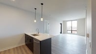This single-floor unit showcases a clean, contemporary design with a thoughtful open-concept layout. The kitchen is a standout feature, equipped with stainless steel appliances including a French door refrigerator, microwave, and range, complemented by white subway tile backsplash, white upper cabinetry, and dark lower cabinets. A large island with a quartz countertop and undermount sink anchors the space, illuminated by stylish pendant lighting. Light wood-tone flooring flows throughout the main living areas, creating a seamless and airy feel. The living area benefits from floor-to-ceiling windows that invite abundant natural light and offer views of the surrounding neighborhood. The bedrooms feature plush carpeting and large windows, providing a comfortable and bright retreat. Two bathrooms serve the unit: one features a walk-in glass-enclosed shower with large-format tile surround, a backlit vanity mirror, and dark wood cabinetry, while the second offers a full soaking tub and shower combination with a matching dark-toned vanity. Light-toned large-format tile flooring ties both bathrooms together cohesively. An in-unit laundry area adds everyday convenience, completing this well-designed modern living space.