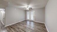 Located at 900 Brookhill Cir in Pell City, Alabama, this single-floor, 2-bedroom, 2-bathroom home offers a well-organized layout with consistent neutral-toned finishes throughout. The living room is highlighted by rich wood-look vinyl flooring, a ceiling fan, and a set of French doors that invite natural light and provide outdoor access. Adjacent to the living area, the dining space features the same flooring and a pendant light fixture, opening directly into the kitchen. The kitchen is laid out in a galley style with white cabinetry, dark granite-style countertops, wood-look flooring, and white appliances including a refrigerator and range. Both bedrooms are carpeted and include ceiling fans and closet storage — the primary bedroom offers a spacious walk-in closet with wire shelving. The two bathrooms are finished with white vanity cabinetry, dark granite-style countertops, and wood-look flooring; one features a shower/tub combination. A dedicated laundry area adds everyday convenience. Textured ceilings are present throughout, and the home's consistent gray palette creates a cohesive, clean aesthetic from room to room.