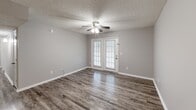 Located at 900 Brookhill Cir in Pell City, Alabama, this single-floor, 2-bedroom, 2-bathroom home offers a well-organized layout with consistent neutral-toned finishes throughout. The living room is highlighted by rich wood-look vinyl flooring, a ceiling fan, and a set of French doors that invite natural light and provide outdoor access. Adjacent to the living area, the dining space features the same flooring and a pendant light fixture, opening directly into the kitchen. The kitchen is laid out in a galley style with white cabinetry, dark granite-style countertops, wood-look flooring, and white appliances including a refrigerator and range. Both bedrooms are carpeted and include ceiling fans and closet storage — the primary bedroom offers a spacious walk-in closet with wire shelving. The two bathrooms are finished with white vanity cabinetry, dark granite-style countertops, and wood-look flooring; one features a shower/tub combination. A dedicated laundry area adds everyday convenience. Textured ceilings are present throughout, and the home's consistent gray palette creates a cohesive, clean aesthetic from room to room.
