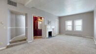 Located on Edgewater Drive in Lakewood, Ohio, this 2-bedroom, 3-bathroom single-floor home offers a generous and thoughtfully arranged layout. The multiple living areas are carpeted throughout and bathed in a neutral gray palette, creating a calm and versatile atmosphere. A standout feature is the elegantly detailed white fireplace with ornate column and carved mantel surpluses, serving as a focal point in one of the main living spaces. Adjacent to the fireplace is a striking built-in bar or display nook finished in rich deep-red wood with arched detailing, adding a warm contrast to the otherwise light interior. Ceiling fans with integrated lighting are found in several rooms, including a living area with a distinctive tray ceiling. The second bedroom is well-proportioned, receiving natural light through large windows and featuring its own ceiling fan. The galley-style kitchen is outfitted with white cabinetry, white appliances, light countertops, and wood-look flooring, complemented by warm yellow walls and a bright window. The bathrooms feature classic blue tile wainscoting, tile flooring, and tub-shower combinations. A private rooftop terrace provides outdoor space with open sky views, a rare and notable amenity for the area.