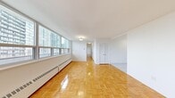 This 1-bedroom, 1-bathroom unit offers a thoughtfully organized layout across a single floor, making efficient use of its compact footprint. Entry is through a tiled hallway that transitions seamlessly into the main living area, where gleaming parquet flooring in a classic basket-weave pattern extends throughout. The living room is a standout feature, characterized by a wide bank of floor-to-ceiling windows that flood the space with natural light and frame expansive urban skyline views. Baseboard heating units run along the perimeter beneath the windows, ensuring year-round comfort.

The kitchen is cleanly designed with white shaker-style cabinetry, grey laminate countertops, a stainless steel double sink, and a stainless steel range, complemented by a window that brings in additional natural light and city views.

The bedroom is a well-proportioned retreat, also featuring parquet flooring, a large window with urban views, and the notable convenience of two double louvered closets, providing generous storage space. A second louvered closet is located in the living area as well.

The bathroom is finished in a clean, contemporary style with a white vanity, grey countertop, an undermount sink, and a mirrored medicine cabinet above. Crisp white walls throughout the unit contribute to a bright, airy ambiance.