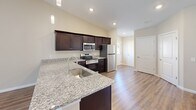 Located at 6102 Vermillion Cedar Way in Kannapolis, NC, this well-appointed single-story home offers 2 bedrooms and 2 bathrooms within a thoughtfully designed open-concept floor plan. The combined kitchen and living area serves as the heart of the home, showcasing vaulted ceilings that lend a sense of openness and volume. Rich hardwood-style flooring runs throughout the main living areas, complemented by warm neutral tones on the walls. The kitchen is equipped with dark espresso cabinetry, granite countertops, a stainless steel appliance suite including a range, microwave, dishwasher, and refrigerator, along with pendant lighting that adds a modern touch. The living room benefits from natural light streaming through large windows and connects seamlessly to the rest of the home. Both bedrooms feature plush carpeting, ceiling fans, and windows that bring in natural light. The primary bedroom is generously sized with its own dedicated closet. Each bathroom is finished with granite-topped dark vanities and hardwood-style flooring — one offering a tub/shower combo and the other a walk-in shower. The attached garage provides ample storage and parking space, completing this functional and stylish home.