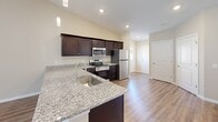 Located at 6102 Vermillion Cedar Way in Kannapolis, NC, this well-appointed single-story home offers 2 bedrooms and 2 bathrooms within a thoughtfully designed open-concept floor plan. The combined kitchen and living area serves as the heart of the home, showcasing vaulted ceilings that lend a sense of openness and volume. Rich hardwood-style flooring runs throughout the main living areas, complemented by warm neutral tones on the walls. The kitchen is equipped with dark espresso cabinetry, granite countertops, a stainless steel appliance suite including a range, microwave, dishwasher, and refrigerator, along with pendant lighting that adds a modern touch. The living room benefits from natural light streaming through large windows and connects seamlessly to the rest of the home. Both bedrooms feature plush carpeting, ceiling fans, and windows that bring in natural light. The primary bedroom is generously sized with its own dedicated closet. Each bathroom is finished with granite-topped dark vanities and hardwood-style flooring — one offering a tub/shower combo and the other a walk-in shower. The attached garage provides ample storage and parking space, completing this functional and stylish home.