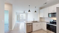 Located at 7301 Topwater Dr in Wilmington, NC, this well-appointed one-bedroom, one-bathroom unit offers a thoughtfully designed open-concept layout that maximizes its efficient footprint. Light wood-style flooring runs throughout, creating a cohesive and bright atmosphere across all rooms.

The kitchen serves as a central focal point, featuring white shaker-style cabinetry extending to the ceiling, a herringbone tile backsplash, quartz countertops, a peninsula with an undermount sink, and a full suite of stainless steel appliances including a French door refrigerator, electric range, microwave, and dishwasher. Pendant lighting accents the peninsula, adding a modern touch. The kitchen flows seamlessly into the living area, which is bathed in natural light from large windows and a glass-paneled door leading to an outdoor balcony. A ceiling fan provides additional comfort.

The bedroom is a well-sized, serene retreat with a large window overlooking greenery and its own ceiling fan. It is complemented by a spacious walk-in closet outfitted with built-in shelving and double hanging rods for ample storage.

The bathroom features a dual-sink vanity with quartz countertops, white cabinetry, a large mirror with overhead lighting, and open shelving. Louvered doors provide access to an in-unit laundry area.