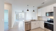 Located at 7301 Topwater Dr in Wilmington, NC, this well-appointed one-bedroom, one-bathroom unit offers a thoughtfully designed open-concept layout that maximizes its efficient footprint. Light wood-style flooring runs throughout, creating a cohesive and bright atmosphere across all rooms.

The kitchen serves as a central focal point, featuring white shaker-style cabinetry extending to the ceiling, a herringbone tile backsplash, quartz countertops, a peninsula with an undermount sink, and a full suite of stainless steel appliances including a French door refrigerator, electric range, microwave, and dishwasher. Pendant lighting accents the peninsula, adding a modern touch. The kitchen flows seamlessly into the living area, which is bathed in natural light from large windows and a glass-paneled door leading to an outdoor balcony. A ceiling fan provides additional comfort.

The bedroom is a well-sized, serene retreat with a large window overlooking greenery and its own ceiling fan. It is complemented by a spacious walk-in closet outfitted with built-in shelving and double hanging rods for ample storage.

The bathroom features a dual-sink vanity with quartz countertops, white cabinetry, a large mirror with overhead lighting, and open shelving. Louvered doors provide access to an in-unit laundry area.