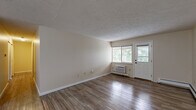 Located at 1908 Newton St in Akron, Ohio, this single-floor, 2-bedroom, 1-bathroom home offers a functional and comfortable layout with a variety of practical features throughout. The living room is a generous, open space with durable hardwood-style flooring, a textured ceiling, and a wall-unit air conditioner. Natural light streams in through a large window and exterior door, offering pleasant views of surrounding greenery. An entry door with direct access adds convenience to the layout. The galley-style kitchen is well-equipped with warm oak cabinetry lining both walls, ample counter space, a stainless steel double-basin sink, and hardwood-style flooring. A pantry provides additional storage, and the kitchen opens into the main living area. Both bedrooms feature plush wall-to-wall carpeting and textured ceilings, with windows overlooking lush outdoor foliage. The primary bedroom is a comfortable size and includes access to a dedicated closet. The shared full bathroom is finished with white square tile surrounding a full-size soaking tub and shower combination, complemented by hardwood-style flooring. Baseboard heating is present throughout, ensuring consistent warmth. The neutral color palette across the home creates a clean, move-in ready atmosphere.