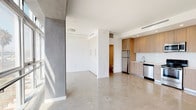 Located at 8155 Van Nuys Blvd in the Panorama City neighborhood of Los Angeles, this modern single-floor unit showcases a clean, contemporary design with an open-concept layout. Polished concrete floors run throughout, lending an industrial-chic aesthetic that complements the crisp white walls and exposed structural elements finished in smooth gray concrete.

The living area is bathed in abundant natural light through expansive floor-to-ceiling windows, offering open views of the surrounding neighborhood. The space feels airy and generous, with a seamless flow between the living and kitchen areas.

The kitchen is well-appointed with light wood cabinetry extending to the ceiling, providing ample storage. A full suite of stainless steel appliances includes a refrigerator, electric range, built-in microwave, and dishwasher, all set against a clean white countertop and backsplash. Recessed lighting and a ceiling-mounted HVAC system ensure comfort throughout the space.

The bathroom features a bright, white subway-tiled tub and shower combination enclosed by a sleek glass door, paired with a white vanity and modern chrome fixtures, creating a clean and polished finish. A built-in closet with paneled doors provides practical storage within the living area. Overall, the unit presents a minimalist, urban aesthetic ideal for modern living.