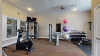 Located at 351 Peat Moss Dr in Columbus, OH, this fitness center offers a comprehensive, single-floor workout facility designed to accommodate a wide range of exercise routines. The space is organized into distinct functional zones, making it easy for users to transition between cardio, strength, and flexibility training.

The cardio area features multiple treadmills, elliptical machines, and stationary bikes arranged along a windowed wall fitted with slatted blinds, allowing natural light to filter into the space. Wall-mounted flat-screen televisions are positioned throughout, providing entertainment during workouts. Structural columns divide sections of the room while maintaining an open, airy feel, and ceiling fans contribute to climate comfort.

The strength and free weights section is well-stocked with a multi-function cable machine, a weight bench, a full rack of kettlebells, and a set of dumbbells in graduated sizes. Stability balls in various sizes are neatly stored on a dedicated stand alongside a balance board.

A separate area includes a mirrored wall, medicine ball rack, and a wall-mounted mini-split HVAC unit for individualized climate control. This zone also features entry access via a paneled door with a coat hook rack nearby. The flooring throughout consists of durable, low-pile carpet in a warm neutral tone, and recessed lighting provides consistent illumination across the entire facility.