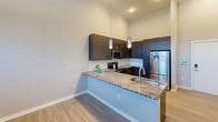 Located at 2120 N Brevard Street in Charlotte's NoDa neighborhood, this one-bedroom, one-bathroom unit offers a well-designed layout with modern finishes across a single floor. The open kitchen serves as a centerpiece of the living space, showcasing dark espresso cabinetry, granite countertops, a subway tile backsplash, and a full suite of stainless steel appliances including a refrigerator, range, and microwave. A peninsula with an undermount sink and pendant lighting above creates a natural division between the kitchen and living area, making it ideal for both cooking and entertaining. Soaring ceilings amplify the sense of openness throughout the unit, complemented by light wood-style flooring that flows seamlessly through the main living areas. The bedroom offers a comfortable footprint with plush carpeting and a large frosted-glass panel that diffuses natural light while maintaining privacy. The bathroom is finished with matching granite countertops, dark cabinetry, a full tub-shower combination lined with classic white subway tile, and open shelving for convenient storage. A hallway with tall ceilings connects the bedroom, bathroom, and closet, reinforcing the unit's overall sense of height and airiness. Clean, neutral tones throughout create a cohesive and contemporary aesthetic.