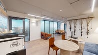 Located at 420 East Ohio Street in Chicago's vibrant Streeterville neighborhood, this single-floor professional space offers a compact yet highly functional layout finished with contemporary design sensibilities throughout.

The open-plan interior is divided into several distinct functional zones. A welcoming lounge area features a pair of cognac leather armchairs flanking sleek round side tables, set against a full-height frosted glass partition wall that diffuses light while maintaining privacy. Adjacent to this is a comfortable banquette seating area with a blue upholstered sofa, warm wood accent chairs, and round tables — ideal for informal meetings or collaborative work. A curated gallery wall of framed artwork and a decorative woven wall hanging lend a creative, studio-like ambiance.

A central workstation area is anchored by a light wood communal table with built-in power access and blue task chairs, positioned beneath suspended linear lighting fixtures. The integrated kitchenette features white cabinetry, a sink, and a microwave, providing full day-use convenience. Light oak hardwood flooring runs continuously throughout, unifying the space and enhancing its bright, airy feel. Recessed and track lighting ensures excellent illumination across all zones.