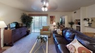This single-floor residence offers a cohesive and inviting interior defined by warm tones, consistent finishes, and practical design throughout. The living room serves as the heart of the home, featuring plush carpeting, a ceiling fan, and a full-width sliding glass door that opens to a private patio, filling the space with natural light and outdoor views. Adjacent to the living area, the dedicated dining space accommodates a full-size table and is finished with a chandelier overhead, creating a defined area for meals and gatherings. The kitchen is equipped with a double-basin stainless steel sink, coil-burner range, ample wood cabinetry, and speckled laminate countertops, with a convenient pass-through window connecting it to the living area. Two bedrooms provide comfortable retreats, each fitted with ceiling fans and carpeted floors. The primary bedroom features a textured ceiling and natural light from a window with draping curtains. Both bathrooms are functional and well-maintained — one features hardwood-style flooring, a shower-tub combo, and a single vanity, while the other offers a larger vanity with granite-style countertops, a bold framed mirror, and a shower-tub with curtain. Throughout, the warm wood cabinetry and earthy color palette create a unified, welcoming atmosphere.