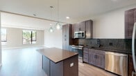 Located at 299 DeBaliviere Ave in St. Louis, MO, this thoughtfully designed single-floor unit offers a seamless open-concept layout that connects the kitchen and living area in a bright, airy environment. Light hardwood flooring flows continuously throughout, complementing the clean, neutral color palette.

The kitchen serves as the heart of the space, showcasing rich dark-toned shaker cabinetry accented by matte black hardware, a striking vertical tile backsplash, and dark countertops. A large central island with a warm wood-toned surface provides additional workspace and is highlighted by a pair of elegant teal glass pendant lights. Stainless steel appliances, including a gas range, microwave, dishwasher, and refrigerator, complete the well-appointed kitchen.

The expansive living area receives generous natural light through large windows that frame views of the surrounding St. Louis neighborhood. The bedrooms feature tall, slim windows that bring in additional daylight. Bathrooms are finished to a high standard, with the primary bath offering a dual-sink vanity with white countertops, dark wood cabinetry, matte black fixtures, and a large mirror. A secondary bathroom provides a single-sink vanity with consistent finishes. The overall design reflects a modern, cohesive aesthetic throughout.