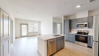 This well-appointed 3-bedroom, 3-bathroom unit in Oxford, Mississippi offers a clean, modern aesthetic across a thoughtfully designed single-floor layout. The open-concept living and kitchen area serves as the heart of the home, where light wood-style flooring flows seamlessly throughout. The kitchen is a standout feature, equipped with slate-blue shaker-style cabinetry reaching toward the ceiling, bright white quartz countertops, a white subway tile backsplash, and a full suite of stainless steel appliances including a refrigerator, range, and built-in microwave. A central island with an integrated sink and dishwasher provides additional prep space and casual seating potential. The adjacent living area benefits from generous natural light through large windows and direct access to an exterior door. Each of the three bedrooms offers a calm, neutral palette with light flooring and ceiling fans or ample overhead lighting. Select bedrooms include closets with built-in shelving systems for organized storage. The three bathrooms are finished consistently, featuring gray vanity cabinetry with white countertops and tiled tub-shower combinations with large-format neutral tile surrounds. Two dedicated closets further enhance the unit's storage capacity. The overall ambiance is bright, clean, and contemporary.