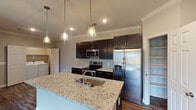 This single-story, 2-bedroom, 2-bathroom home in Beaumont, TX offers a thoughtfully designed open-concept layout with consistent, modern finishes throughout. Rich wood-look flooring flows seamlessly across the living, dining, and kitchen areas, complemented by crown molding and recessed lighting that enhance the clean, contemporary aesthetic.

The kitchen is a standout feature, showcasing dark espresso cabinetry, light granite countertops, a classic subway tile backsplash, and a full suite of stainless steel appliances. A large center island with an undermount sink and pendant lighting above serves as both a functional workspace and a natural gathering point. An adjacent pantry provides generous storage.

The open living area is anchored by a ceiling fan with light kit and offers a clear sightline to a conveniently located in-unit laundry area. Both bedrooms are well-sized, each featuring wood-look flooring, ceiling fans, and windows with blinds that allow natural light while maintaining privacy.

The two bathrooms mirror each other in style, featuring dark cabinetry with granite-topped vanities, wood-framed mirrors, subway tile tub surrounds, and soaking tubs. Every detail reflects a cohesive, modern design sensibility throughout this move-in-ready home.