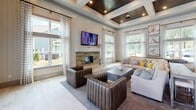 Located at 50 Cheryl Lane in Summerville, SC, this single-story community clubhouse is designed with a refined yet welcoming aesthetic that blends modern farmhouse and coastal influences throughout. The grand great room serves as the heart of the space, boasting soaring coffered ceilings with rich wood inlays, recessed lighting, and an eye-catching stone fireplace flanked by a wall-mounted TV. Expansive windows dressed in crisp striped drapery flood the room with natural light and offer views of the surrounding greenery, creating an airy, open ambiance. The fully equipped community kitchen features slate-blue shaker cabinetry, white quartz countertops, a mosaic tile backsplash, a large center island with seating, stainless steel appliances, and dramatic industrial-style pendant lighting. A dedicated conference room provides a functional gathering space with a rustic wood table, classic Windsor-style chairs, shiplap-accented walls, and a wall-mounted display screen. The entry foyer is appointed with large-format tile flooring and framed nature-inspired artwork, with glass double doors that open directly to the outdoor pool area. The cohesive design palette, featuring neutral tones, warm wood accents, and curated artwork, lends the entire space a polished yet approachable character.