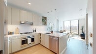 Located at 200 Mesnager St in Los Angeles' Chinatown neighborhood, this modern one-bedroom, one-bathroom residence offers a thoughtfully designed open-concept layout with clean lines and a bright, contemporary aesthetic throughout. Light wood-tone flooring runs seamlessly across the entire space, complementing the soft neutral palette on the walls and cabinetry.

The kitchen is well-appointed with stainless steel appliances, including a gas range, wall oven, and dishwasher, set against sleek taupe cabinetry and white quartz countertops. A peninsula with pendant lighting provides additional prep space and opens directly to the living area, which is anchored by a dramatic exposed concrete architectural column and a large round mirror. The living room is bathed in natural light through expansive floor-to-ceiling windows that frame sweeping views of the Los Angeles skyline and lead to a private balcony.

The bedroom is a calm, well-proportioned retreat featuring a tall window that fills the room with natural light. A dedicated closet provides storage, and the concrete accent detail carries through from the main living space. The bathroom features a full tub-shower combination with white tile surround, a wide vanity with ample counter space, and light wood flooring that maintains the cohesive design language found throughout the home.
