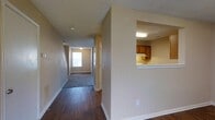 This two-story residence offers a functional and well-organized layout designed for comfortable everyday living. The main level greets you with a long, open hallway finished with rich, dark hardwood-style flooring that extends throughout the primary living spaces. Neutral beige walls and white baseboards provide a clean, cohesive aesthetic that lends itself to a variety of interior styles.

A notable architectural feature on the main level is the pass-through kitchen window, which opens the kitchen to the adjacent hallway and living area. The kitchen is equipped with warm wood-toned cabinetry and overhead lighting, creating a practical and inviting cooking space. The pass-through design promotes an open feel while maintaining a defined kitchen zone.

The hallway leads toward a carpeted living area at the far end of the main floor, where a window allows natural light to filter in, brightening the space. Staircase access to the upper level is conveniently positioned along the hallway, offering a straightforward flow between floors.

The textured ceilings add subtle dimension throughout, while the consistent use of neutral tones across walls and trim creates a harmonious interior atmosphere. Overall, this residence combines practical design with comfortable, livable spaces across both floors.