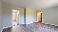 This well-organized 2-bedroom, 1-bathroom unit is laid out efficiently across a single floor, offering a clean and functional living environment. Consistent light gray laminate flooring flows throughout the space, creating a cohesive and contemporary feel.

The open living area greets residents upon entry through a solid white front door with brass hardware. Neutral gray walls and clean white baseboards contribute to a bright, understated aesthetic. The living space connects directly to the kitchen, which features white shaker-style cabinetry extending to the ceiling for generous storage, light speckled countertops, a stainless steel sink, and a full-size refrigerator.

The spacious primary bedroom is a standout feature, offering room for substantial furnishings, two windows that invite natural light and views of surrounding greenery, a ceiling fan, and a radiator for heating. It also includes a double sliding-door closet with built-in shelving for organized storage. The second bedroom is a well-proportioned space with access to an additional closet.

The bathroom is cleanly appointed with a white vanity, a tiled tub-shower combination, wood-look flooring, and a window above the tub that provides natural light and ventilation. A hallway connects the rooms, completing the practical and tidy layout of this space.