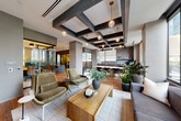 Located in the heart of Atlanta's Midtown neighborhood, this professionally designed coworking space offers a sophisticated blend of open collaboration areas and private workspaces across a single, well-appointed floor. The centerpiece of the space is a spacious open lounge featuring warm hardwood flooring, a striking coffered ceiling with dark acoustic panels, and globe pendant lighting that creates an inviting, upscale ambiance. Large floor-to-ceiling windows flood the lounge with natural light and frame views of the surrounding Midtown skyline, while lush indoor plants add a refreshing natural element throughout.

The lounge is furnished with plush seating arrangements, including olive-toned lounge chairs and a solid wood coffee table, encouraging both relaxed collaboration and informal meetings. Adjacent to the lounge is a well-equipped kitchenette featuring warm wood cabinetry, a central island with a stone countertop, and bar seating — ideal for casual gatherings or breaks.

Multiple private work pods, enclosed with glass-panel partitions and black steel frames, provide quiet, focused workspaces. Each pod is fitted with an adjustable-height desk, a monitor, ergonomic seating, and soft sage-green walls that promote concentration. The seamless balance of open and enclosed areas makes this space highly functional for a variety of professional needs.
