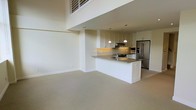 This two-story residence showcases a thoughtfully designed open-concept floor plan that seamlessly connects the living and kitchen areas. The space immediately impresses with its dramatic double-height ceilings, which flood the interior with a sense of openness and grandeur. A loft-style upper level overlooks the main living area below, adding architectural interest and functional versatility.

The kitchen is a standout feature, appointed with crisp white cabinetry that extends to the upper walls, dark stone countertops, and a central island that doubles as a prep area and casual dining space. Stainless steel appliances, including a French door refrigerator and a range with an overhead hood, complete the modern culinary setup. Pendant lighting hangs above the island, providing focused illumination with a clean, contemporary aesthetic.

The open living area is finished with neutral-toned carpeting that lends warmth and comfort underfoot, while the light-colored walls enhance brightness throughout the space. The cohesive, neutral palette creates a versatile backdrop suitable for a variety of interior styles. Overall, the layout and design elements combine to produce a welcoming, functional, and visually striking two-level home.