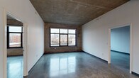 This single-floor urban loft showcases a striking industrial-modern aesthetic defined by exposed concrete ceilings, polished concrete floors, and crisp white walls that create a bold visual contrast throughout. Large black-framed windows dominate several rooms, framing expansive views of the surrounding cityscape and flooding the interiors with natural light. The open living areas are generously proportioned, with the raw concrete ceiling adding an authentic industrial character and a sense of architectural depth.

The kitchen is thoughtfully designed with white shaker-style upper cabinetry paired with warm wood-toned lower drawers, white quartz countertops, a stainless steel sink, and a full suite of stainless steel appliances including a refrigerator, range, and over-the-range microwave. Pendant lighting adds a refined finishing touch above the counter.

The bedrooms continue the loft aesthetic with polished concrete floors and city-facing windows framed by exposed concrete surrounds. Two well-appointed bathrooms feature the same warm wood cabinetry, white quartz vanity tops, undermount sinks, brushed nickel fixtures, and tub-shower combinations with white tile surrounds. The overall ambiance is contemporary and urban, balancing raw industrial materials with clean, modern finishes.
