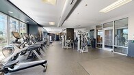 Located at 301 Commons Park S in Stamford, Connecticut, this expansive fitness center offers a comprehensive workout environment spread across a generously sized single floor. The facility is thoughtfully designed with a modern aesthetic, featuring dark navy accent walls, wood-paneled columns, and durable rubber flooring throughout that provides both safety and comfort underfoot.

The cardio zone is well-appointed with a full lineup of professional-grade Cybex treadmills and elliptical trainers, positioned to take advantage of large floor-to-ceiling windows that flood the space with natural light and offer pleasant outdoor views of surrounding greenery. The strength training area features an extensive array of Cybex cable machines, selectorized weight machines, and functional training equipment, including a dual-cable crossover station, providing options for a complete full-body workout.

A dedicated functional training zone features interlocking floor mats, resistance bands, stability balls, and free weights, supporting stretching and bodyweight exercises. Wall-mounted televisions offer entertainment throughout the space. Glass-paneled partitions and doors create a sense of openness while subtly defining distinct training zones. The facility is well-lit through a combination of recessed lighting and large skylights, contributing to an energizing and motivating atmosphere ideal for fitness enthusiasts of all levels.