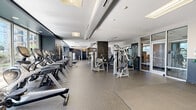 Located at 301 Commons Park S in Stamford, Connecticut, this expansive fitness center offers a comprehensive workout environment spread across a generously sized single floor. The facility is thoughtfully designed with a modern aesthetic, featuring dark navy accent walls, wood-paneled columns, and durable rubber flooring throughout that provides both safety and comfort underfoot.

The cardio zone is well-appointed with a full lineup of professional-grade Cybex treadmills and elliptical trainers, positioned to take advantage of large floor-to-ceiling windows that flood the space with natural light and offer pleasant outdoor views of surrounding greenery. The strength training area features an extensive array of Cybex cable machines, selectorized weight machines, and functional training equipment, including a dual-cable crossover station, providing options for a complete full-body workout.

A dedicated functional training zone features interlocking floor mats, resistance bands, stability balls, and free weights, supporting stretching and bodyweight exercises. Wall-mounted televisions offer entertainment throughout the space. Glass-paneled partitions and doors create a sense of openness while subtly defining distinct training zones. The facility is well-lit through a combination of recessed lighting and large skylights, contributing to an energizing and motivating atmosphere ideal for fitness enthusiasts of all levels.