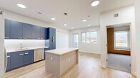 Located at 501 Orleans St in Richmond, VA, this modern one-bedroom, one-bathroom unit offers a well-designed open floor plan with contemporary finishes. The combined kitchen and living area serves as the heart of the space, showcasing bold navy-blue flat-front cabinetry, white quartz countertops, stainless steel appliances including a French door refrigerator, electric range, and dishwasher, complemented by a white tile backsplash. A central kitchen island provides additional prep and dining space, while light wood-tone flooring and recessed ceiling lighting enhance the bright, airy atmosphere. Sliding glass doors lead to a private balcony with wood-plank decking and metal railing, offering open views of the surrounding Richmond neighborhood. The bedroom features plush carpeting, a ceiling fan, a built-in wood wardrobe with integrated storage, and a window with natural light. The unit also includes two closets and an in-unit laundry area for added convenience. The full bathroom is finished with matching navy cabinetry, a dual-sink white vanity, large-format tile flooring, and a tub-shower combination enclosed by a frameless sliding glass door, maintaining a clean, cohesive modern aesthetic throughout.