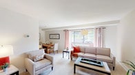 This single-floor residence offers a thoughtfully arranged layout that balances comfort and functionality across its key living areas. The open-plan living and dining space serves as the heart of the home, filled with natural light streaming through large sliding glass doors dressed with patterned curtains. The living area accommodates generous seating and a distinctive coffee table, while views of lush greenery outside create a pleasant indoor-outdoor connection. Adjacent to this is a dedicated dining space with a warm wood table, seamlessly integrated into the flow of the room. The kitchen features rich, warm-toned wood cabinetry providing ample storage, complemented by white appliances including a refrigerator and range, and a stainless steel sink. Light-colored flooring keeps the space feeling bright and clean. The bedroom is a serene retreat, complete with plush carpeting, a window with natural light, a closet with bifold doors, and room for a dresser and full-sized bed. Decorative wall art and carefully chosen accents give the room a cozy, curated ambiance. The bathroom includes a full-sized tub and shower combo with tile surround, accented by classic striped wall detailing. Throughout the residence, neutral tones and soft carpeting in the main living areas create a warm, welcoming atmosphere.