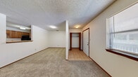 This well-organized 1-bedroom, 1-bathroom single-floor unit offers a functional and comfortable layout across a compact but efficiently designed floor plan. The combined kitchen and living area forms the heart of the unit, with the living room featuring plush wall-to-wall carpeting, a textured ceiling, and a standout tile-surround fireplace with a dark mantel that serves as a focal point. A window with blinds allows natural light to fill the space. The galley-style kitchen is outfitted with warm wood cabinetry on both sides, ample counter space, a double-basin sink, a refrigerator, dishwasher, and a range with overhead ventilation — all set on durable tile flooring. The bedroom is a generously proportioned room with soft carpeting, a large sliding glass door with vertical blinds that invites natural light, and direct access to a dedicated closet. The full bathroom includes a single-sink vanity with wood cabinetry, a toilet, and a full tub-shower combination with tile surround, finished with neutral tile flooring. Throughout the unit, dark wood trim accents provide consistent character, and the textured ceilings tie the spaces together with a cohesive, classic aesthetic.