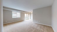 This single-floor residence offers a thoughtfully laid-out living space with a neutral color palette of soft grays and warm beige tones throughout. The expansive main living area is finished with plush wall-to-wall carpeting and features a ceiling fan, a large window fitted with horizontal blinds, and sliding glass doors that open onto a private balcony — allowing an abundance of natural light to fill the room. The open layout connects seamlessly to the rest of the unit, providing a sense of spaciousness and easy flow between areas.

The kitchen is outfitted with warm oak cabinetry that extends to the upper walls, offering generous storage capacity. Speckled laminate countertops provide ample workspace, and the kitchen includes a full suite of white appliances — a refrigerator, dishwasher, and range — set atop light hardwood-style flooring that contrasts warmly with the cabinetry.

The bedrooms continue the home's consistent aesthetic, featuring the same soft carpeting and neutral gray walls. Each room benefits from natural light via blinds-fitted windows and includes access to closet space. Clean white baseboards and trim throughout add a crisp, finished look. The unit's straightforward, functional design makes it a comfortable and adaptable living space.