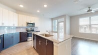 This single-floor residence presents a contemporary open-concept design with a cohesive, neutral color palette throughout. The kitchen serves as a central highlight, featuring a large island with granite countertops and an integrated sink, two-tone cabinetry combining dark espresso lower cabinets with crisp white upper cabinets, a classic subway tile backsplash, and a full suite of stainless steel appliances including a refrigerator, range, microwave, and dishwasher. Wood-look plank flooring connects the kitchen seamlessly to the adjacent living and dining areas, where large windows and a glass-paneled door flood the space with natural light and provide access to the outdoors.

The bedrooms feature plush wall-to-wall carpeting and sets of tall, triple-panel windows that bring in abundant natural light while offering exterior views. Ceiling fans are installed in both the bedroom and living areas for added comfort.

Two bathrooms serve the residence. The primary bathroom includes a dual-sink granite vanity with dark espresso cabinetry, a soaking tub, and wood-look tile flooring. The secondary bathroom features a glass-enclosed walk-in shower with marble-style tile surround and matching wood-look flooring. Both bathrooms maintain a clean, modern aesthetic consistent with the rest of the home.