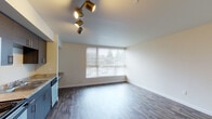 Located at 15th Ave S, Unit 305 in Seattle's 98108 neighborhood, this single-floor residence offers a clean, modern aesthetic throughout. Rich wood-look laminate flooring flows continuously across the living areas, creating a warm and cohesive feel. The open living space is brightened by a large window fitted with blinds, allowing natural light to fill the room while maintaining privacy. Track lighting adds a contemporary touch overhead.

The kitchen is thoughtfully designed with dark, textured cabinetry paired with granite-style countertops, offering ample storage and workspace. Stainless steel appliances include a range, over-the-range microwave, and dishwasher, complemented by a double-basin sink. A built-in countertop extension provides additional prep or dining space.

The bathroom is clean and functional, featuring a full soaking tub with shower, a vanity with mirror, and neutral-toned walls that enhance the bright, airy atmosphere. A closet with built-in shelving and a hanging rod offers practical storage solutions adjacent to the main living area.

The layout, as revealed in the dollhouse view, is efficiently organized, with distinct zones for living, cooking, and bathing — making this a practical and comfortable Seattle residence.